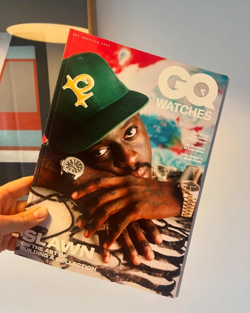 GQ Watches magazine cover featuring a man in a green cap and watches, held in a person's hand, with geometric art in the background.