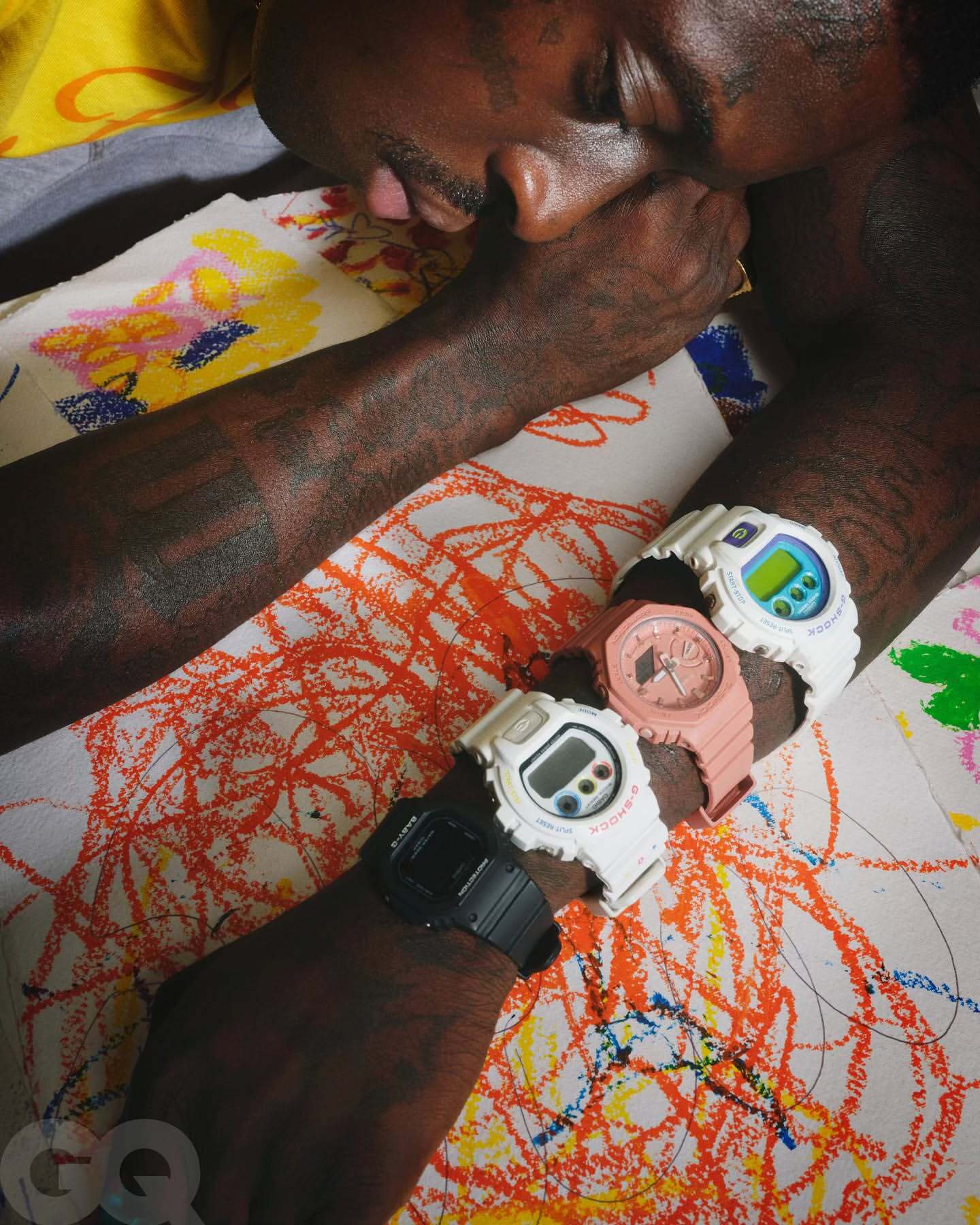 Close-up of a man's arm displaying four wristwatches on an abstract patterned background; wristwatches are black, white, pink, and blue.