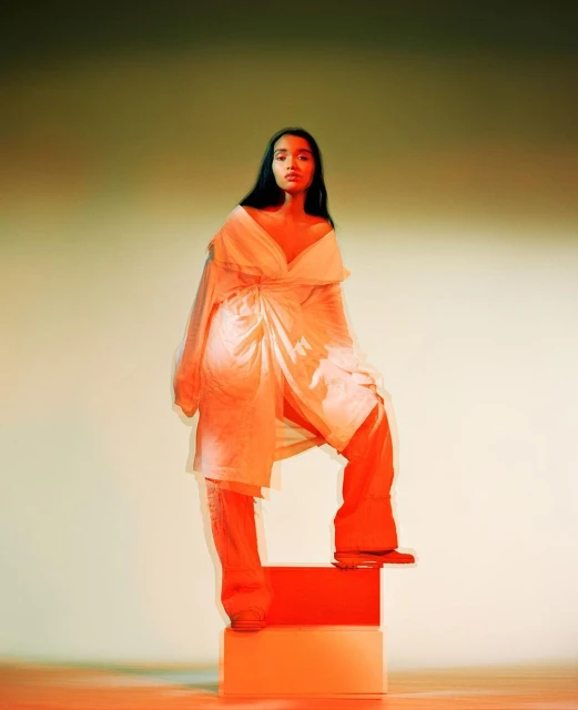 Portrait of a woman in a white outfit posing on colorful blocks, highlighted with vibrant orange and yellow lighting in a studio setting.