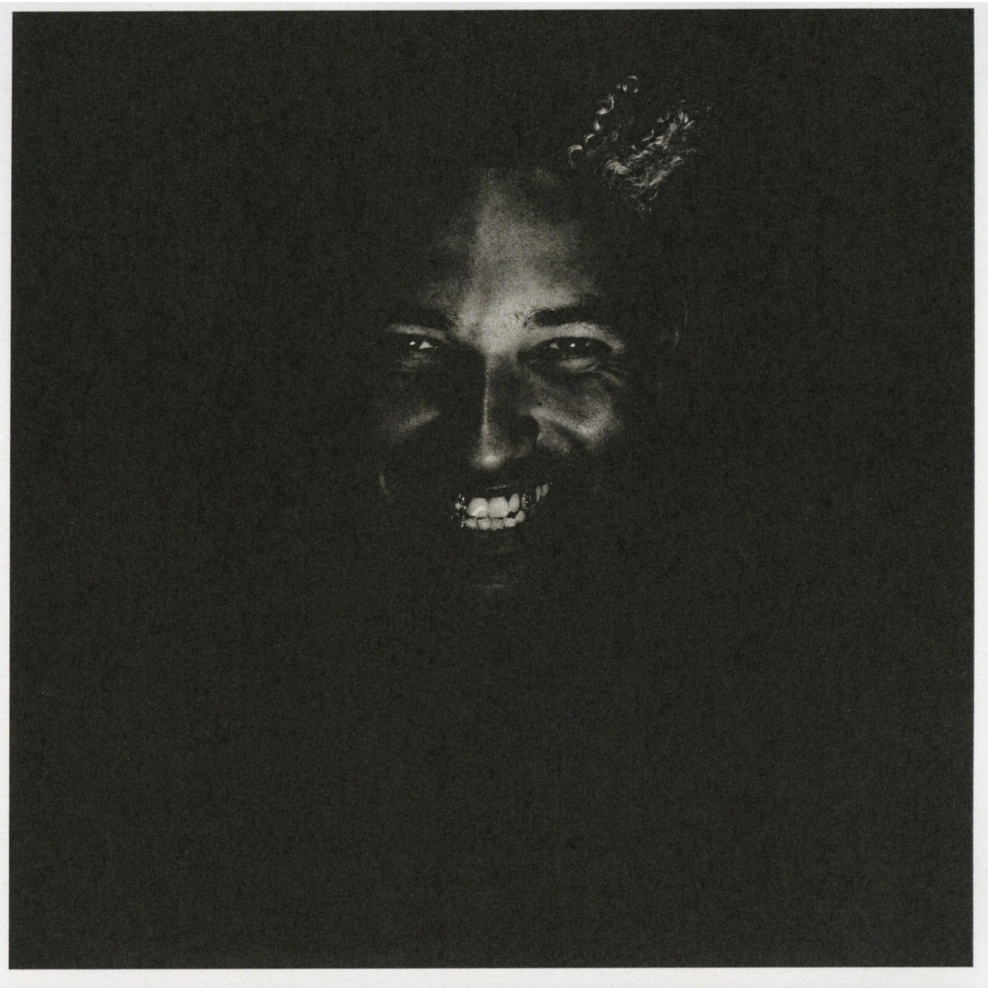 Close-up portrait of a smiling man emerging from deep shadows with heavy film grain and high contrast lighting.