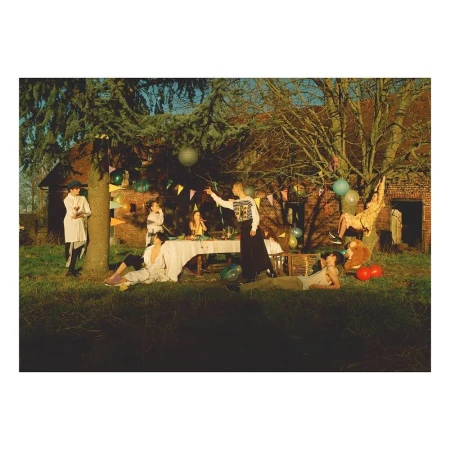 A group of seven young adults in an outdoor setting with a picnic table, balloons, and trees, set against a rustic building backdrop.