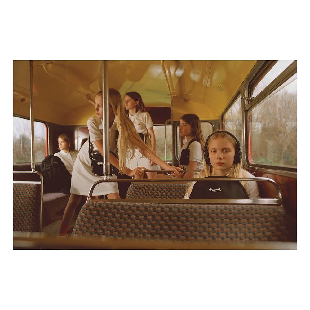 Multiple young girls inside a vintage bus, wearing matching white dresses and black accessories, creating a cohesive and nostalgic image.