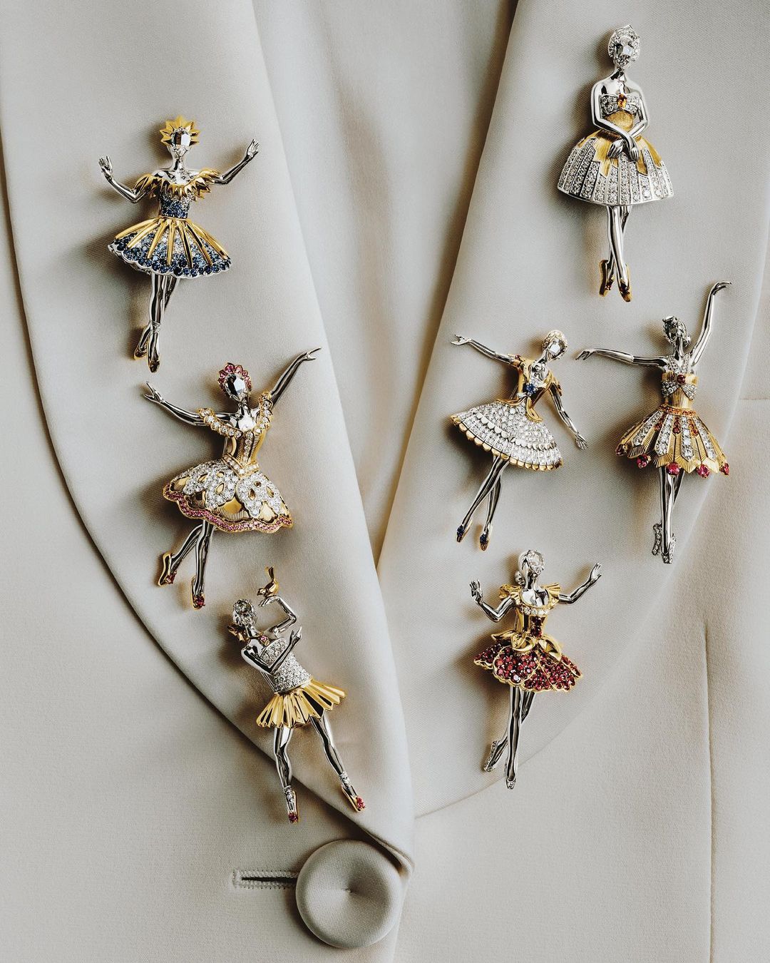 Elegant ballet dancer brooches adorn a light jacket, featuring silver and gold tones with jewel-toned skirts, showcasing artistry and detail.