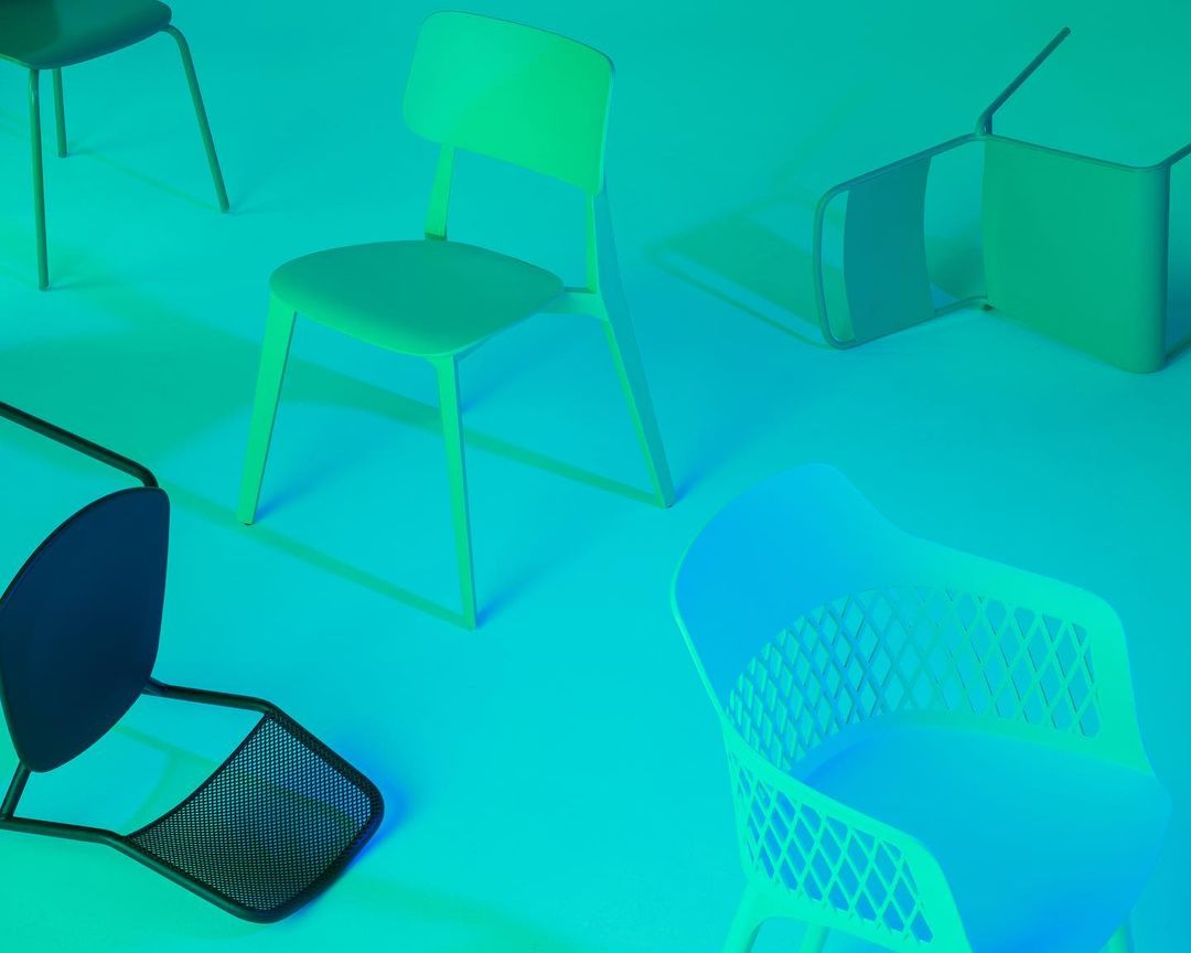 Several chairs of various designs and colors, including green and blue, are arranged in a bright, evenly lit studio setting.