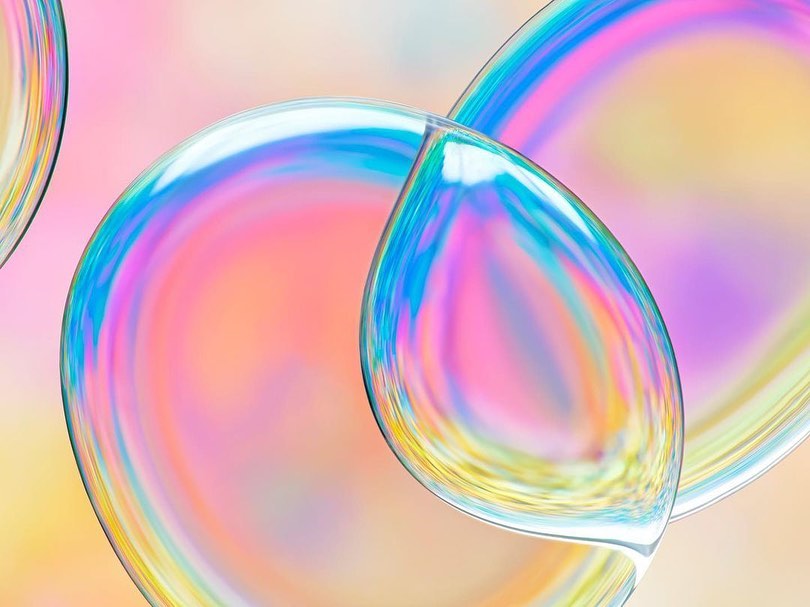 Abstract macro photography of iridescent bubbles with pastel colours. The bubbles have a raindrop shape and layered appearance.