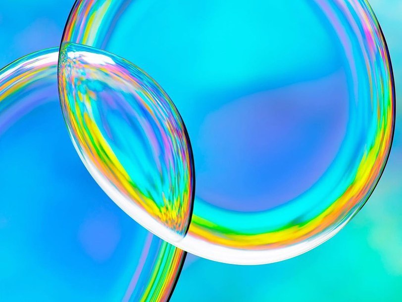 Abstract iridescent bubbles with rainbow refraction patterns on a light blue background.