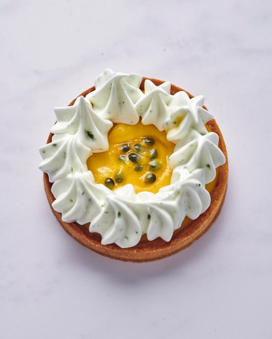 Overhead shot of a passion fruit tart with a cookie crust and meringue frosting, set against a white marble backdrop.
