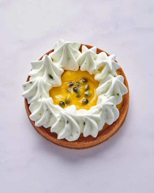 Overhead shot of a passion fruit tart with a cookie crust and meringue frosting, set against a white marble backdrop.
