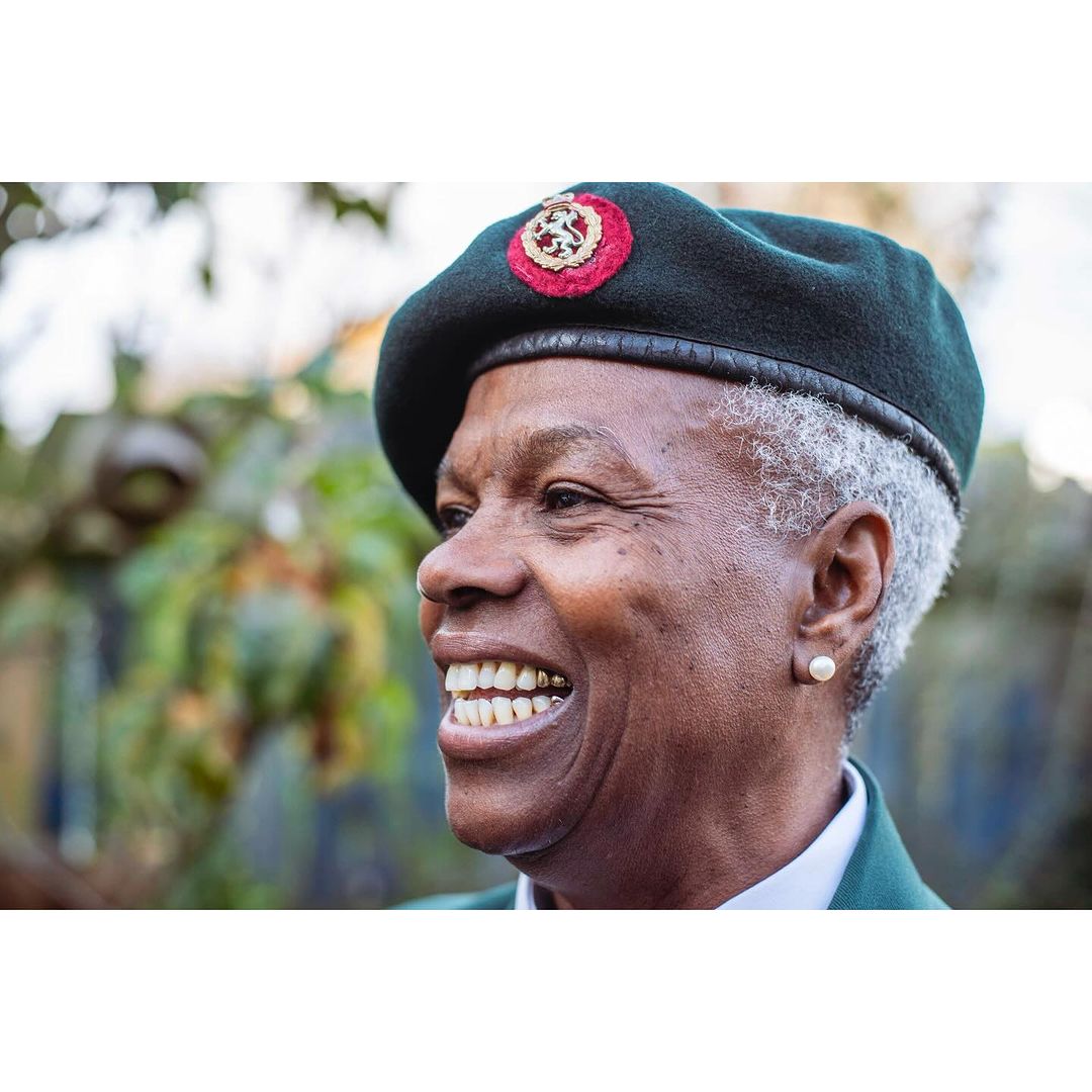 Smiling older adult female wearing a beret outdoors, medium shot. Head and shoulders of woman in green jacket looking to the left.