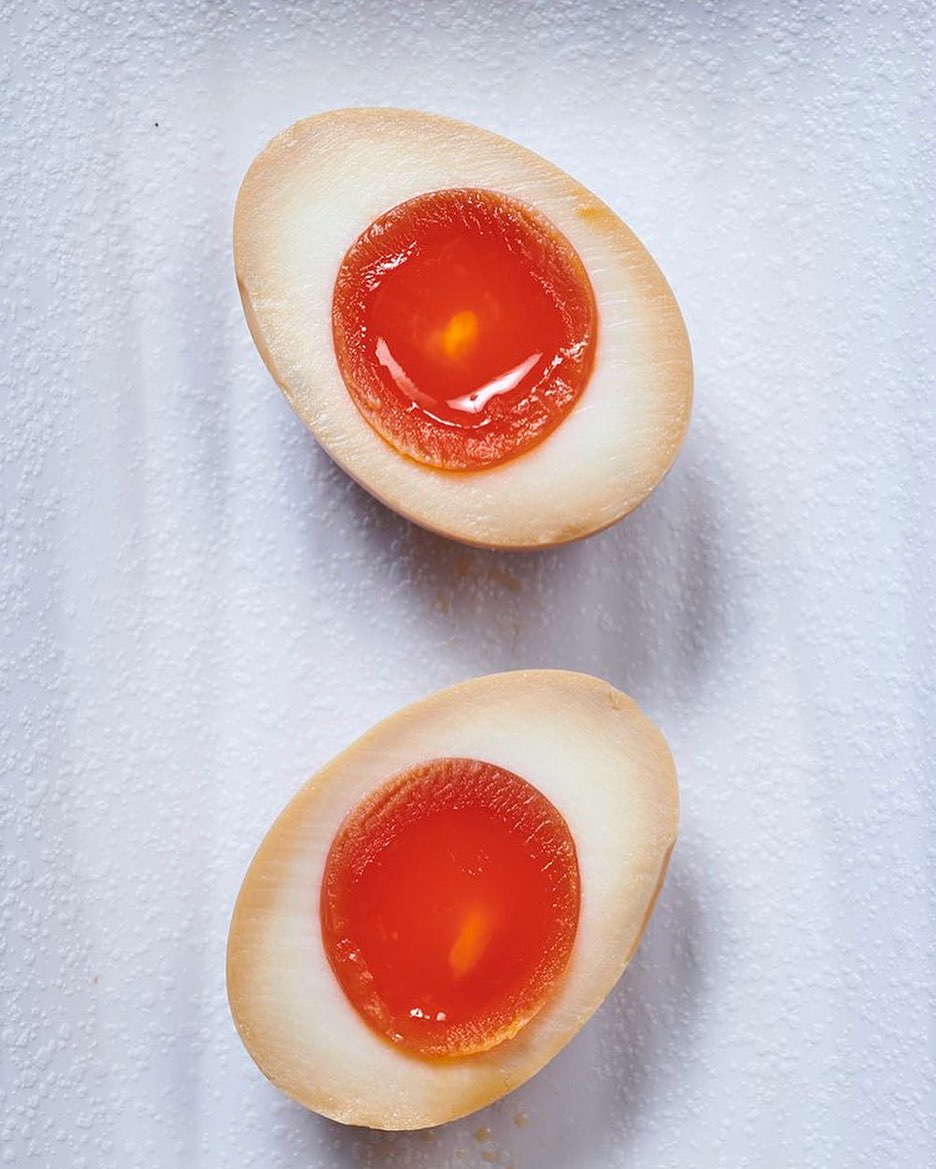 Two halves of a marinated egg with a rich orange yolk are staged on a wrinkled white surface, creating a culinary close-up.
