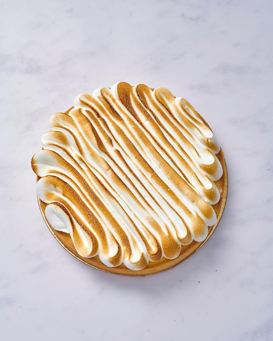 Overhead shot of a lemon meringue tart on a white marble surface, featuring golden-brown toasted meringue topping.