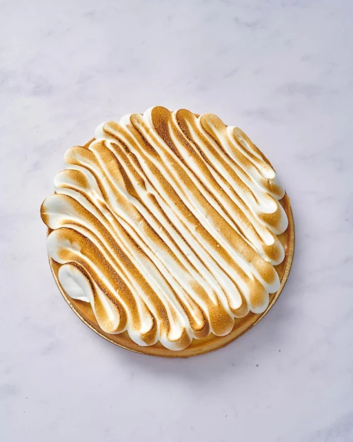 Overhead shot of a lemon meringue tart on a white marble surface, featuring golden-brown toasted meringue topping.
