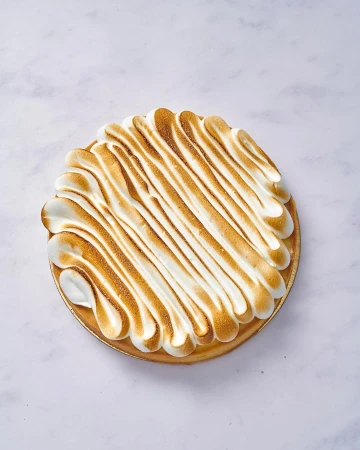 Overhead shot of a lemon meringue tart on a white marble surface, featuring golden-brown toasted meringue topping.