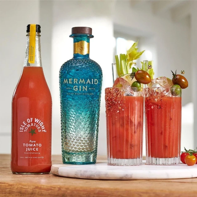 Tomato juice and gin cocktails with celery stalks and tomato garnish on marble board against white wall in indoor setting.