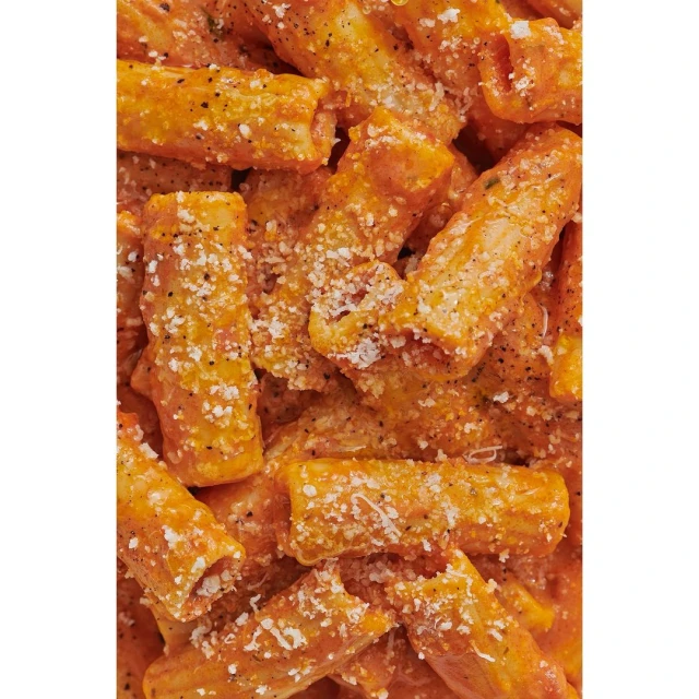 Close-up of rigatoni pasta with a creamy orange sauce and grated cheese topping. Culinary photography of Italian cuisine.