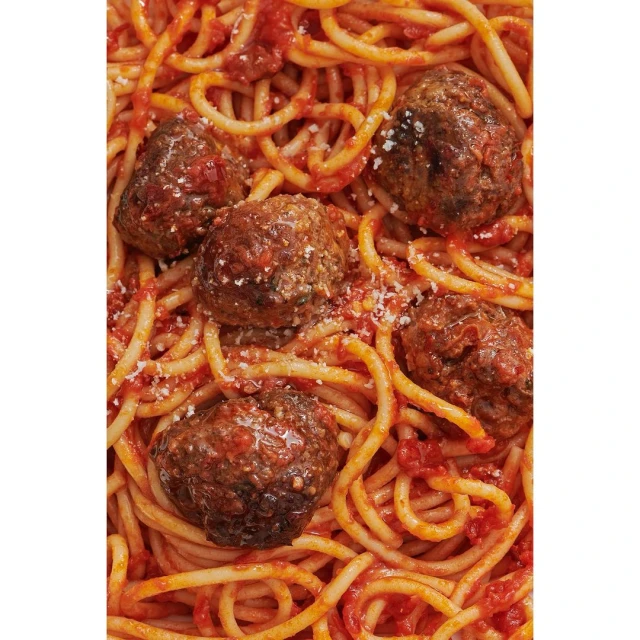 Overhead shot of spaghetti with tomato sauce and five meatballs, sprinkled with parmesan cheese in an indoor setting.