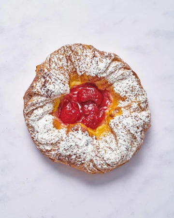 Overhead shot of a freshly baked pastry filled with a red fruit filling and dusted with powdered sugar on a light marble surface.
