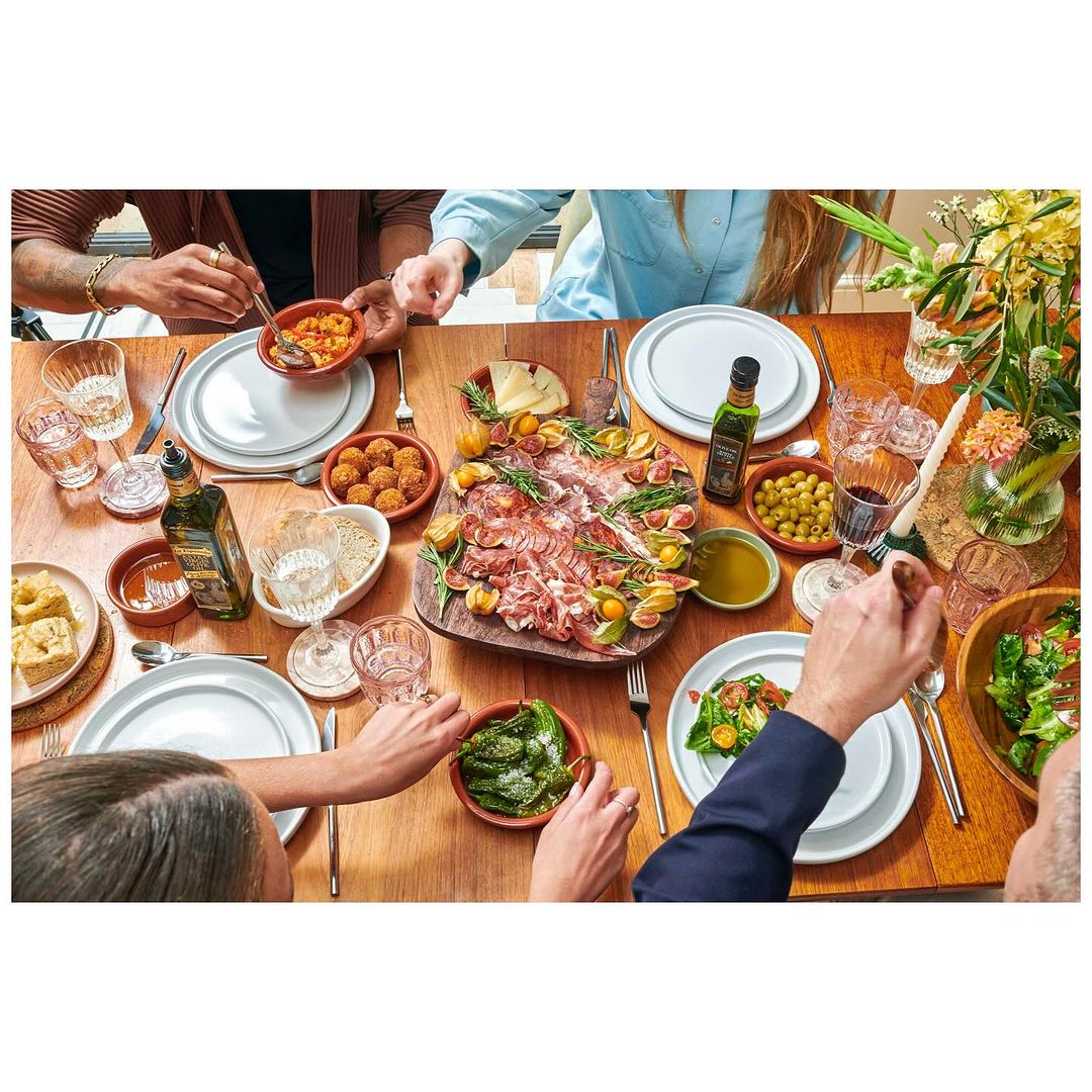 Overhead shot of a group of people dining at a wooden table filled with an assortment of Spanish tapas, olives, and drinks.