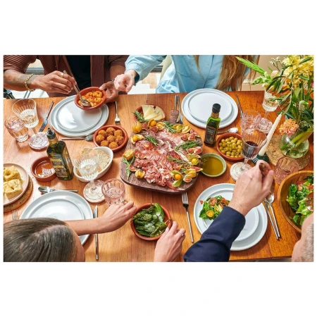 Overhead shot of a group of people dining at a wooden table filled with an assortment of Spanish tapas, olives, and drinks.