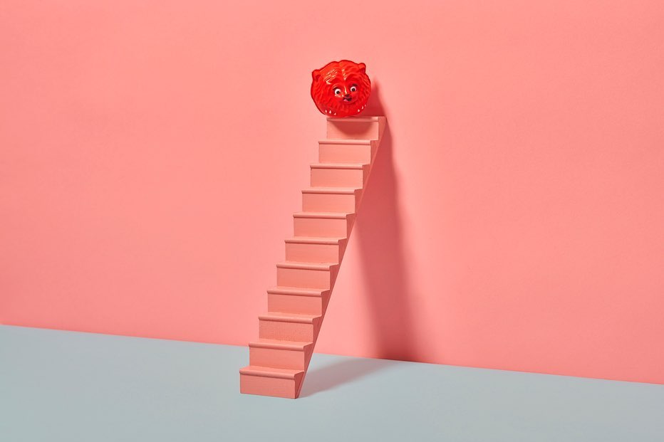 Conceptual image features a red cartoon character atop a pink staircase against a two-tone pink and light blue background for playful art.