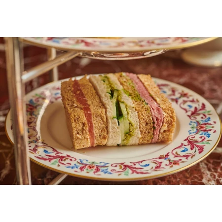 Afternoon tea: stacked sandwiches on a floral plate atop a multi-tiered stand. Focus on fresh, colourful sandwiches.