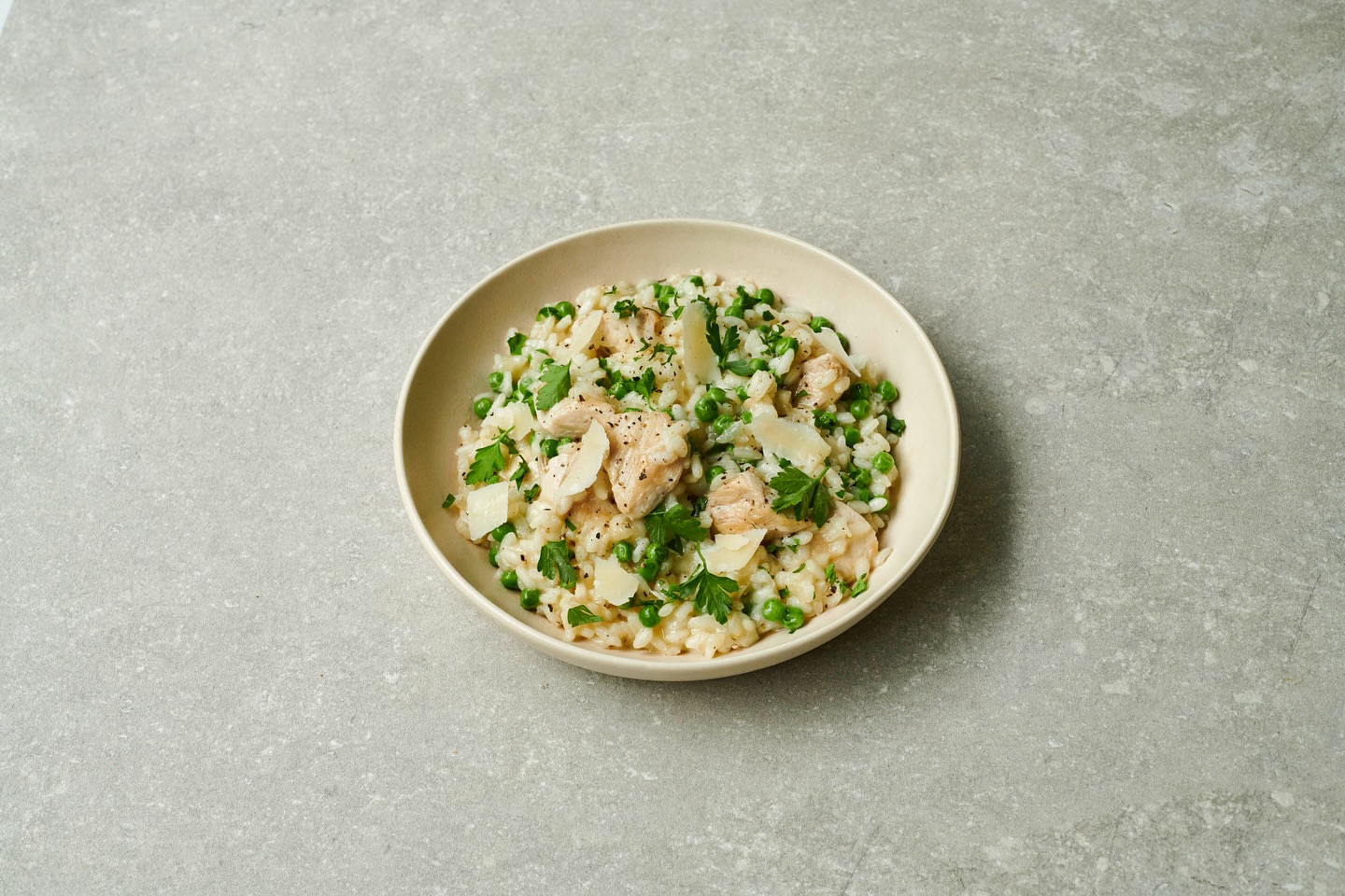 Overhead shot of a bowl of risotto with peas, cheese, and salmon on a gray surface, showcasing food photography and culinary presentation.