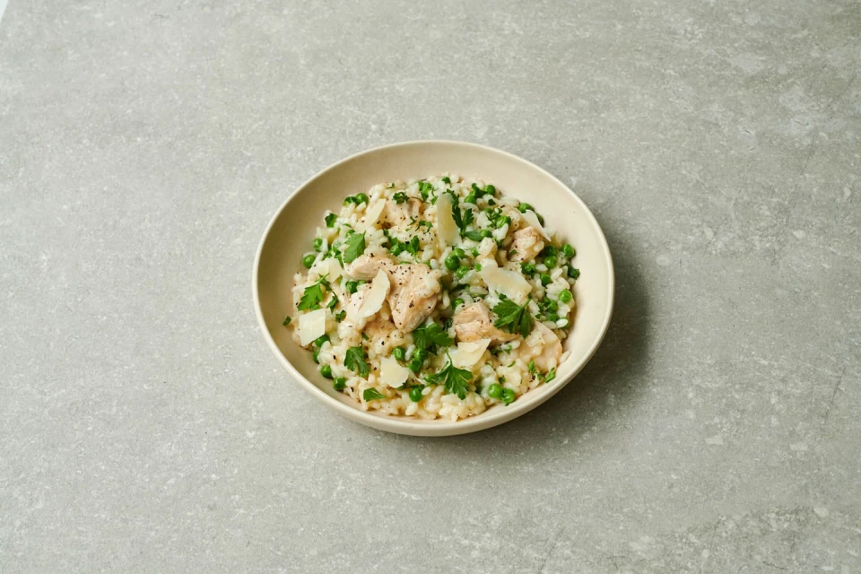 Overhead shot of a bowl of risotto with peas, cheese, and salmon on a gray surface, showcasing food photography and culinary presentation.
