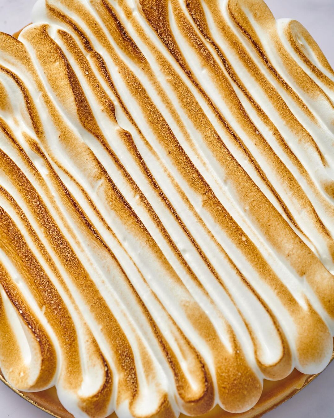 Overhead close-up of a lemon meringue pie, showcasing the toasted meringue peaks and golden-brown crust on a light background.