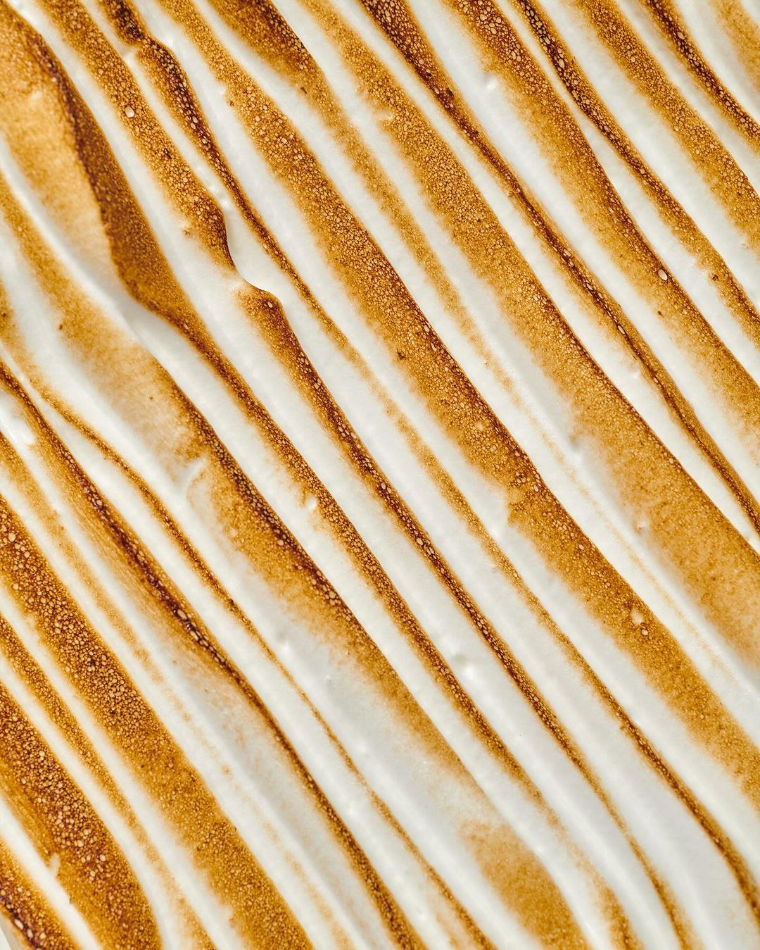 Overhead shot of torched meringue topping with toasted stripes; golden-brown peaks and swirls on white, creamy dessert surface.