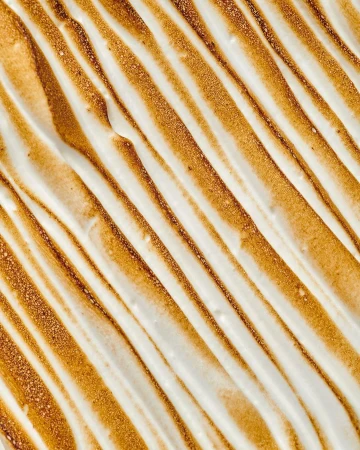 Overhead shot of torched meringue topping with toasted stripes; golden-brown peaks and swirls on white, creamy dessert surface.