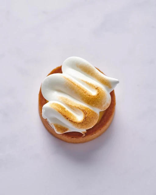 Overhead shot of a single lemon meringue tart on a white surface, showcasing the pastry crust and the torched meringue topping.