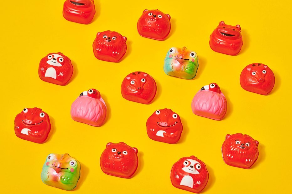 Overhead shot of red and pink animal-shaped toys scattered on a bright yellow background. The composition is bright, colorful, and playful.