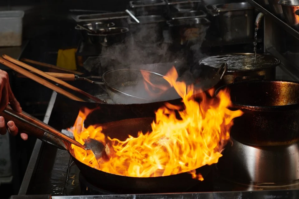 Chef cooking with flames in a wok in a restaurant kitchen. Fire is large and bright under the wok.