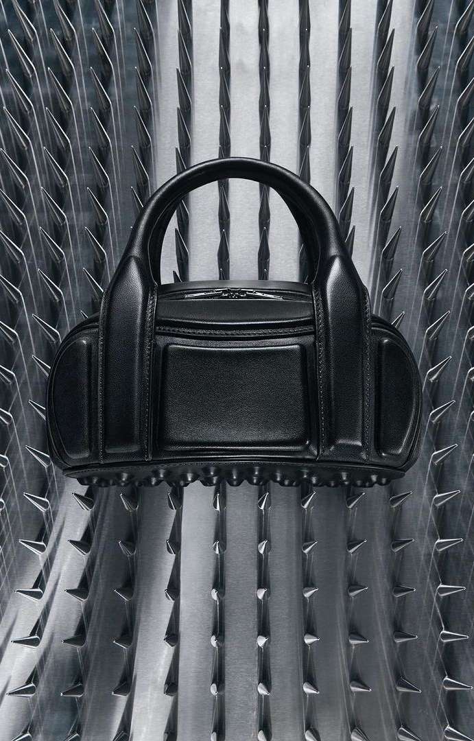 Black leather purse with studded trim displayed against a metallic background with vertical triangular spike details. Fashion accessory.