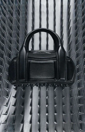 Black leather purse with studded trim displayed against a metallic background with vertical triangular spike details. Fashion accessory.