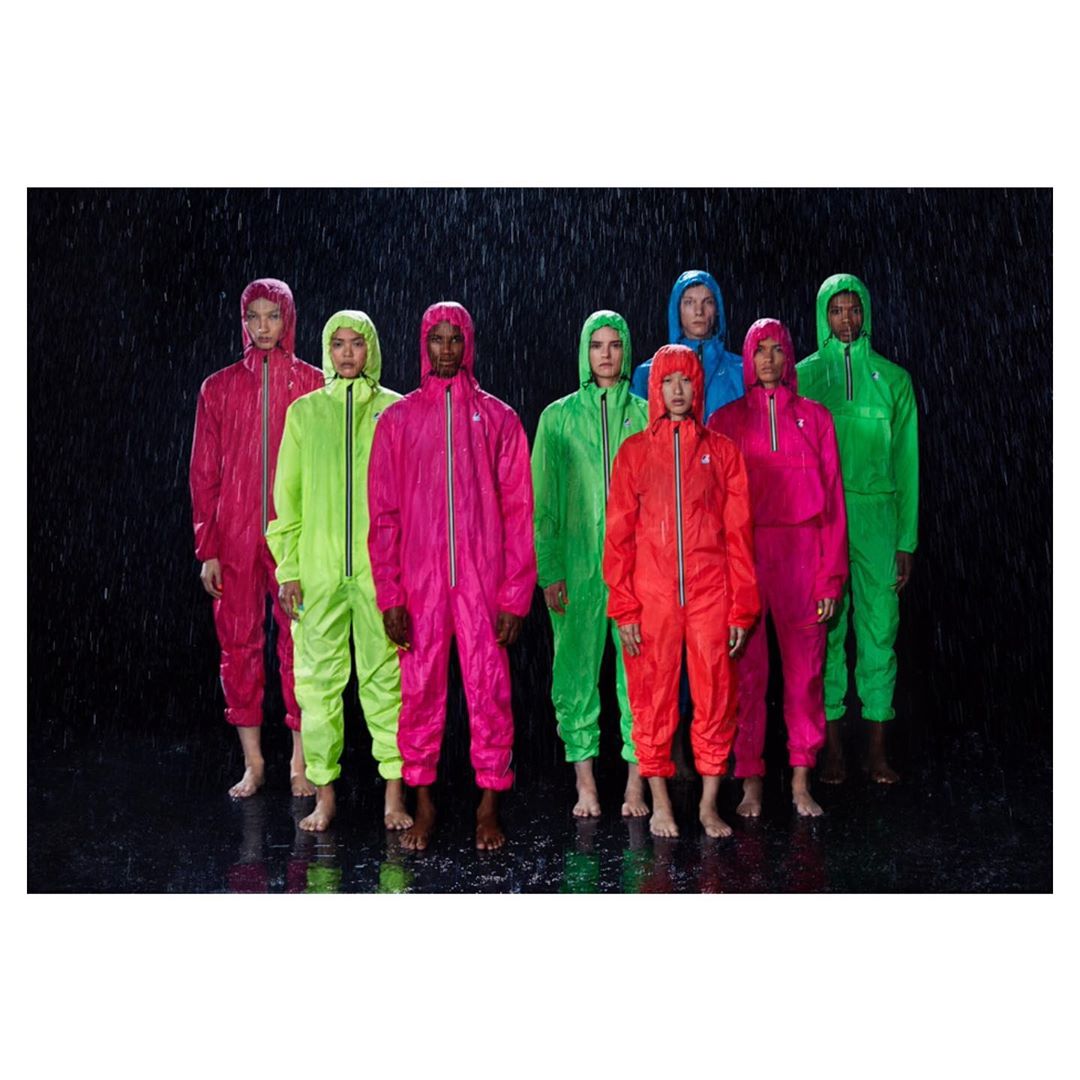 Group of eight people wearing bright colored waterproof hooded jumpsuits in a dark wet environment, fashion promotion, and outdoor apparel.