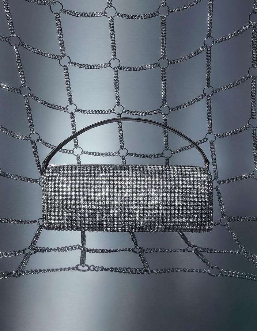 Glamorous handbag with handle sparkling in the spotlight, suspended within a metallic chain-link network. Fashion, glamour, and style.