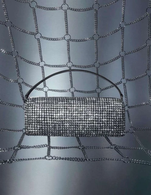 Glamorous handbag with handle sparkling in the spotlight, suspended within a metallic chain-link network. Fashion, glamour, and style.