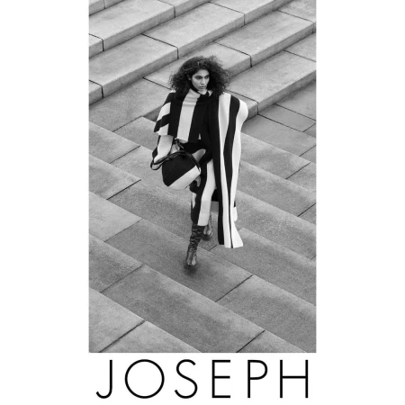 Black and white fashion shot: A woman in a striped poncho and boots walks down a concrete staircase carrying a matching handbag.