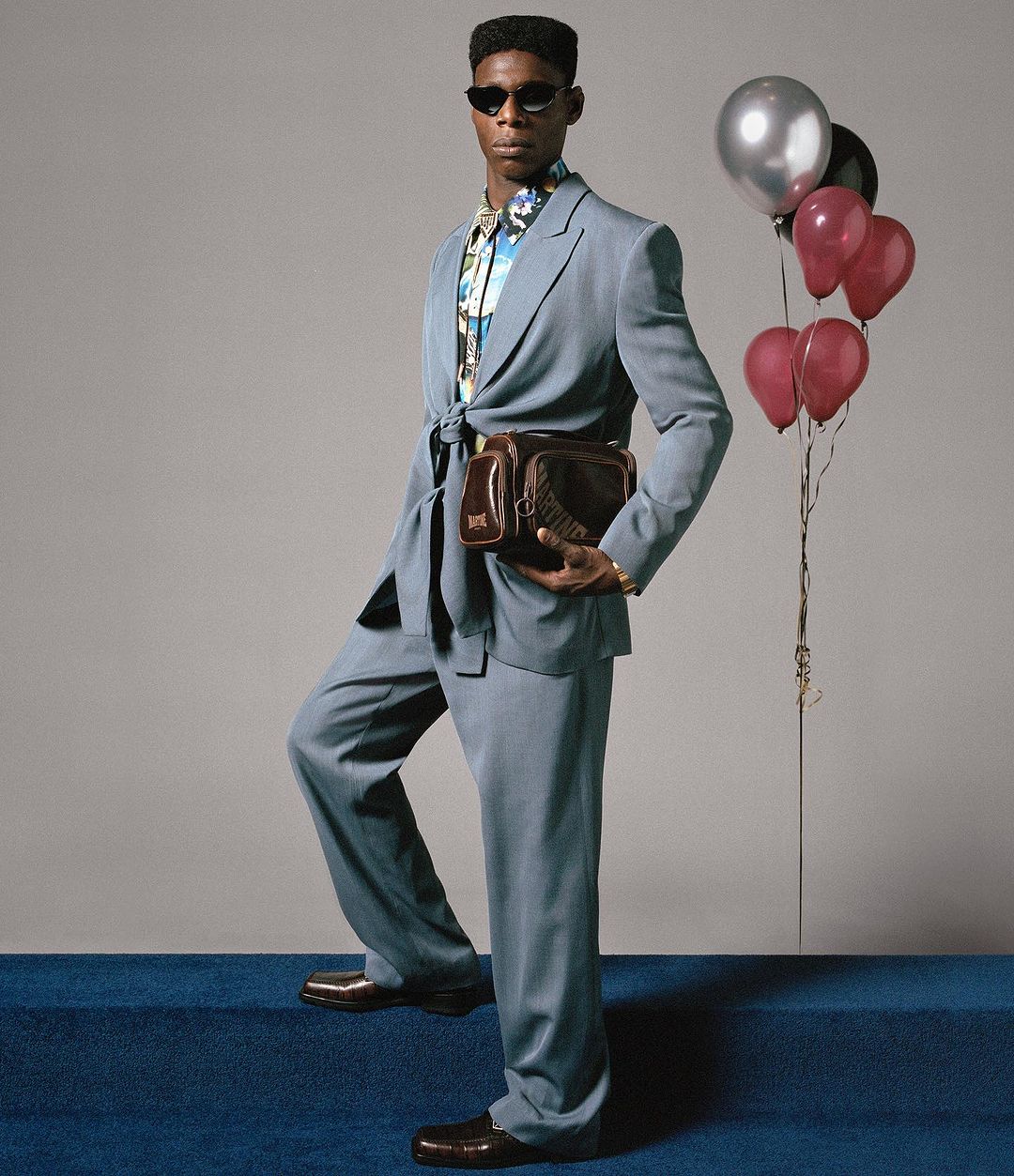 Stylish adult male poses in a blue suit with balloons. Indoor studio shot on blue carpet with neutral backdrop. Fashion and portrait shot.