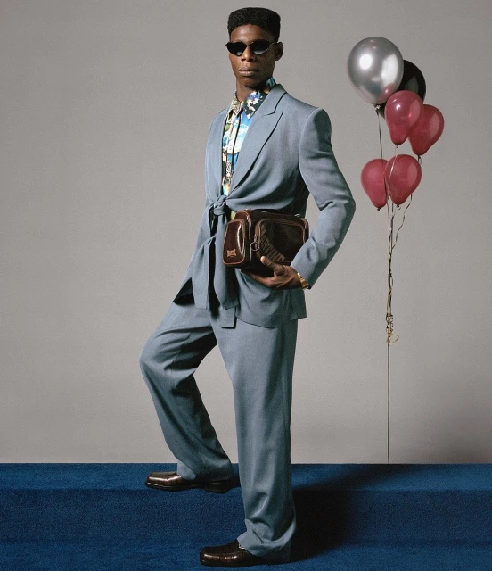 Stylish adult male poses in a blue suit with balloons. Indoor studio shot on blue carpet with neutral backdrop. Fashion and portrait shot.