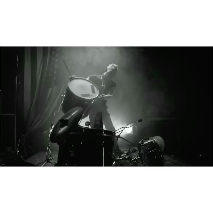 Monochrome shot of a male drummer performing on stage with his drum kit amidst smoke and lights, creating a dynamic musical scene.