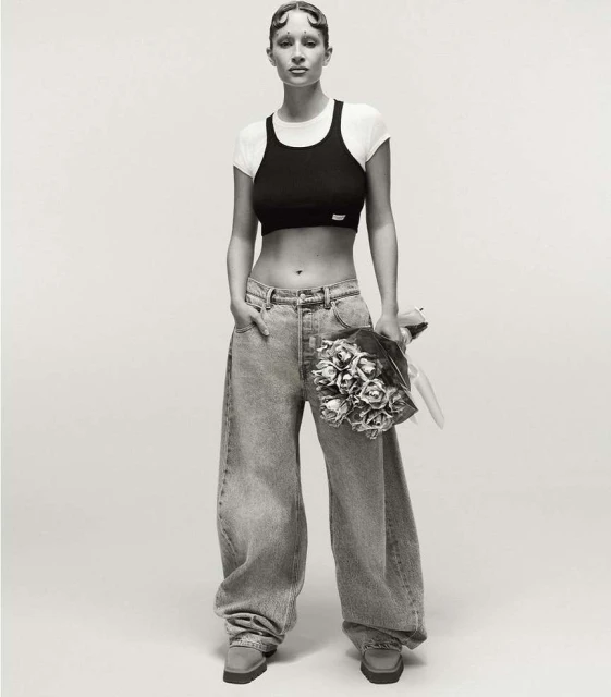 Studio shot of a young woman posing with a bouquet, wearing a black crop top, white t-shirt, baggy jeans, and platform shoes.
