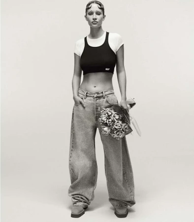 Studio shot of a young woman posing with a bouquet, wearing a black crop top, white t-shirt, baggy jeans, and platform shoes.
