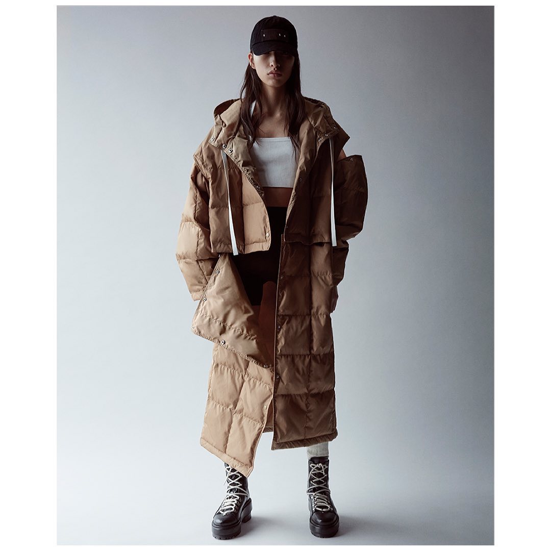 A stylish, full-length studio shot features an adult female model wearing a quilted beige puffer coat, black cap, and platform boots.