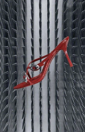 Elevated shot of a glossy red stiletto-heeled sandal against an abstract silver background with metal spike accents and studio lighting.