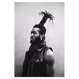 Portrait of a black man with sculpted dreadlocks, nose ring, and leather vest against a plain light background by Jamie Morgan