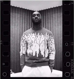 Black and white medium shot of Virgil Abloh wearing a numbered graphic sweatshirt against a textured curtain background