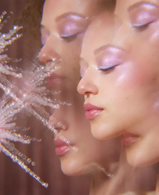 Close-up beauty shot features a light-skinned young adult woman with a shimmering lavender eyeshadow and glossy pink lipstick.