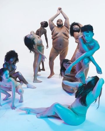 A group of nine diverse adults pose in a semi-circle against a white backdrop, creating a visually striking composition with neutral skin tones.